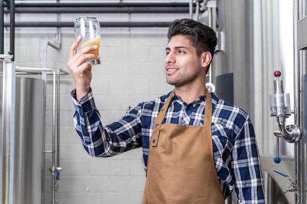 Handsome brewer in apron testing beer at brewery