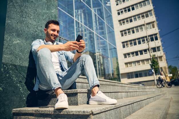 Handsome brunette male person keeping smile on his face while answering on message