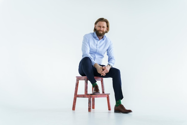 A handsome brutal bearded and longhaired man a stylish businessman sitting on a chair with a white