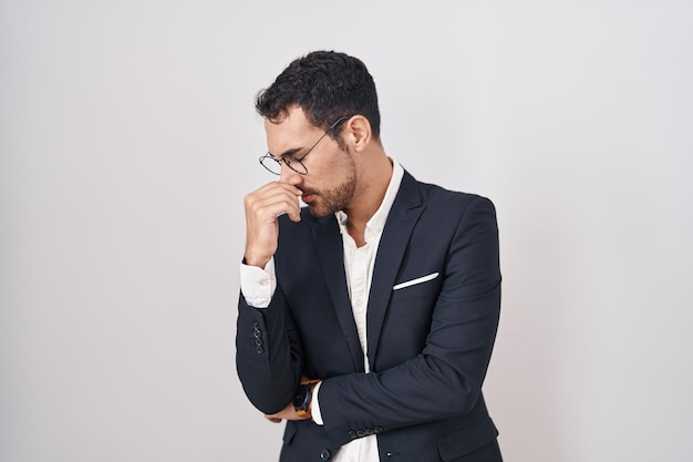 Handsome business hispanic man standing over white background tired rubbing nose and eyes feeling fatigue and headache. stress and frustration concept.