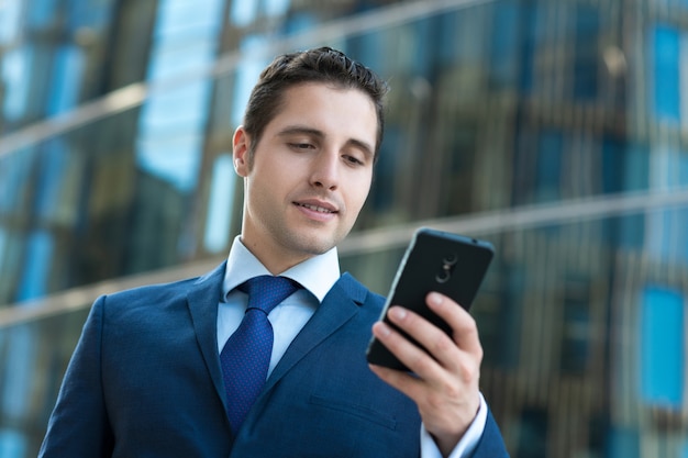 Handsome business man in suit texting message in front of modern building