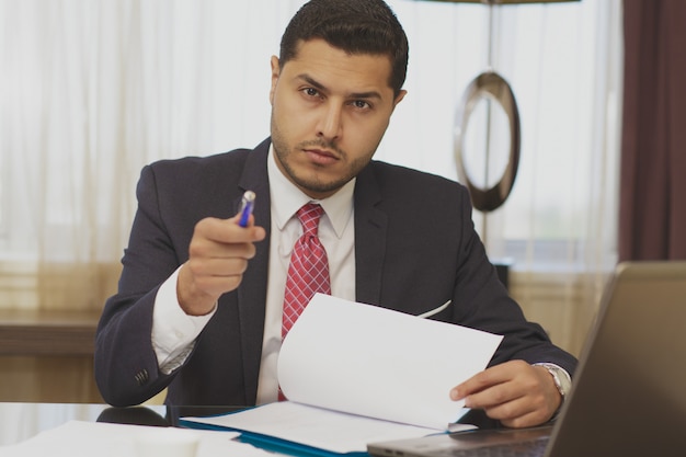 Handsome businessman doing some paperwork and using his laptop