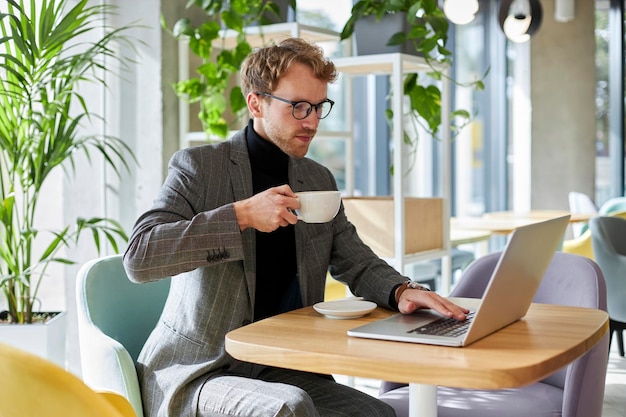 Handsome businessman drinking coffee using laptop computer working online planning startup