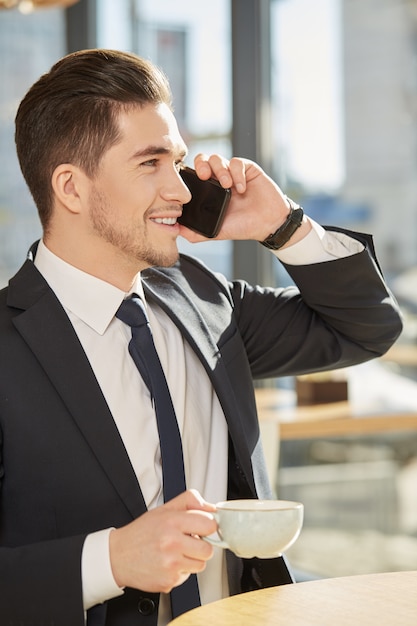 handsome businessman enjoying his coffee talking on the phone smiling happily 