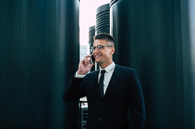 Handsome businessman in full black suit talks on his smart phone at the cityscape background