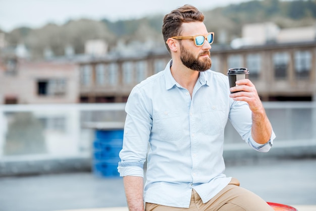 Handsome businessman having a coffeebreak on the rooftop on the industrial background