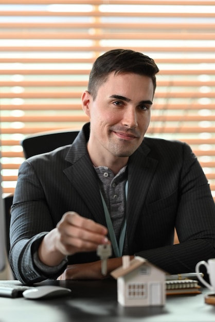 Handsome businessman holding house keys and smiling to camera Mortgage and real estate investment concept