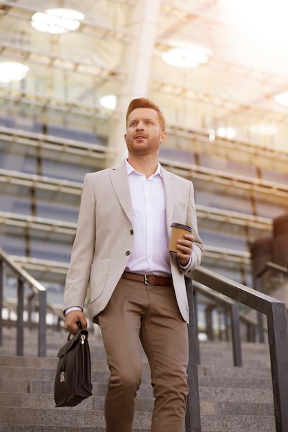 Handsome businessman looking away and keeping coffee in hand while going down the stairs