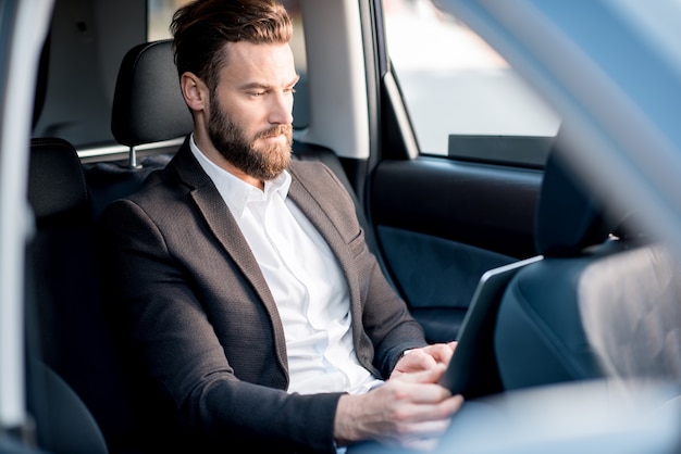 Handsome businessman sitting with laptop on the backseat of the car