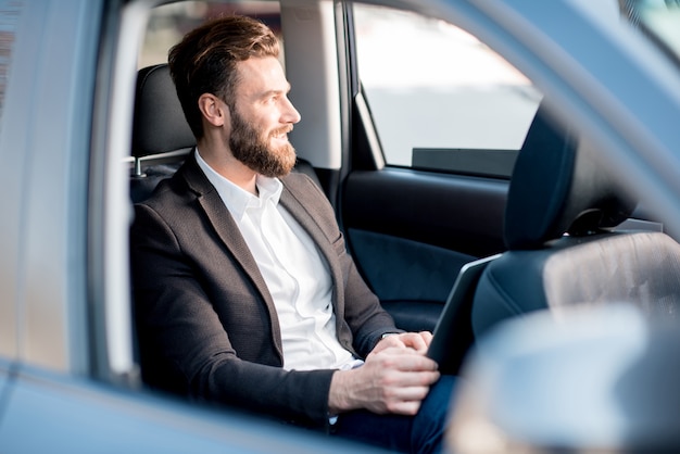 Handsome businessman sitting with laptop on the backseat of the car