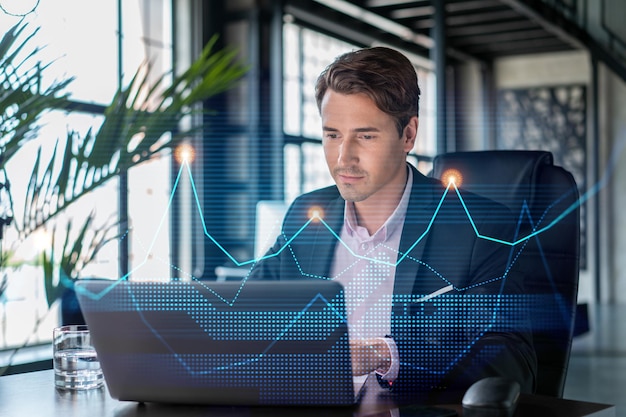 Handsome businessman in suit at workplace working with laptop to optimize trading strategy at corporate finance fund Forex chart hologram over office background