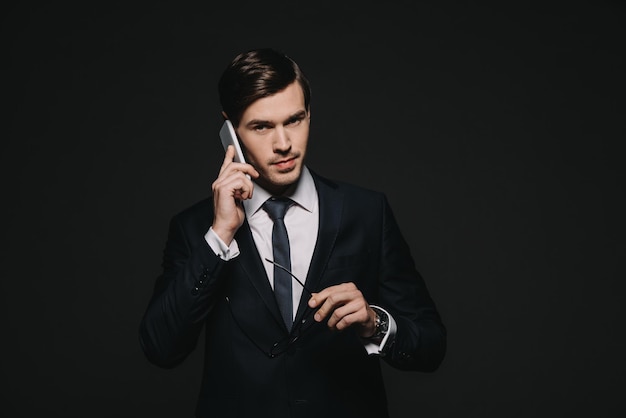 Handsome businessman talking on smartphone isolated on black