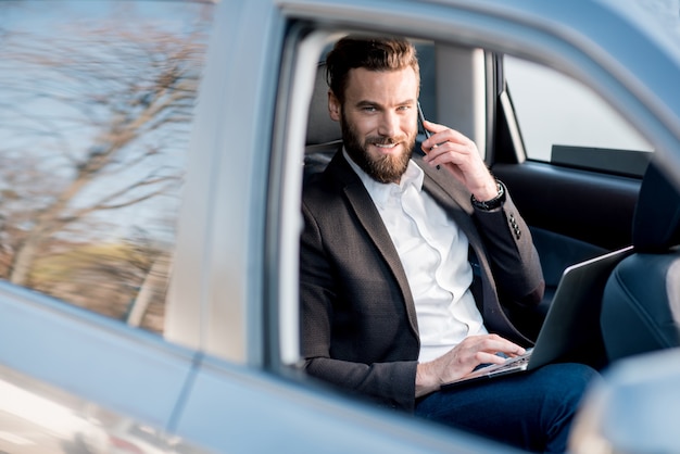 Photo handsome businessman talking with phone sitting on the backseat of the car