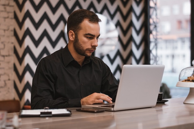 Handsome businessman using laptop at city cafe.