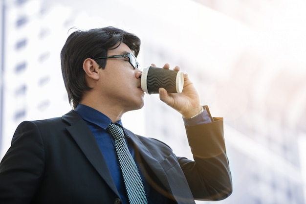 Handsome businessman with paper coffee cup over office building under the sunlight