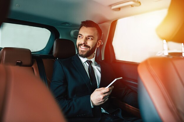 Handsome businessman with phone on hand sitting on the backseat of the car guy looking away