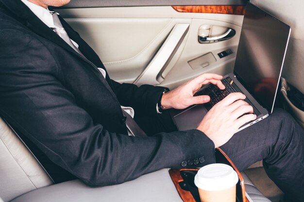 Handsome businessman working on laptop computer sitting on back seat of a car