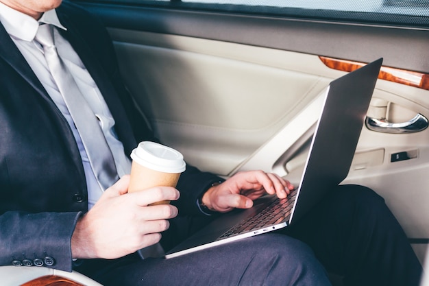 Handsome businessman working on laptop computer sitting on back seat of a car