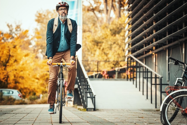 A handsome casual middle-aged businessman is going to the office by bicycle. He is driving bike in front of office district.