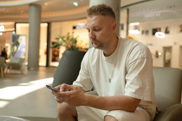 Photo handsome caucasian adult man in stylish casual clothes using mobile phone on a soft chair at