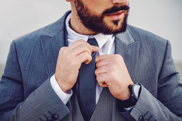 Handsome Caucasian bearded businessman in suit fixing his tie.