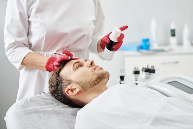 Handsome Caucasian young man at cosmetology procedures in beauty parlor at the beautician Male dermatologist skin care closeup face mask