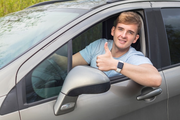 Handsome cheerful guy, driver, young positive man, driving his car, smiling show thumb up, like gesture from automobile window. Happy buyer, customer of a new car enjoying driving. Good buy, purchase