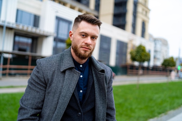 Handsome and cheerful young businessman dressed in formal clothes Male in coat is looking to the camera with city view background