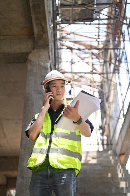 Handsome civil engineer manager standing at construction site and having phone conversation