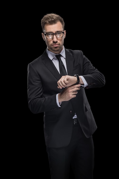 Handsome confident businessman in black suit with watch isolated on black