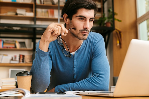 Handsome confident young man sitting at the library desk