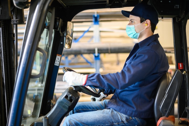 A handsome construction worker driving a forklift in an industrial plant