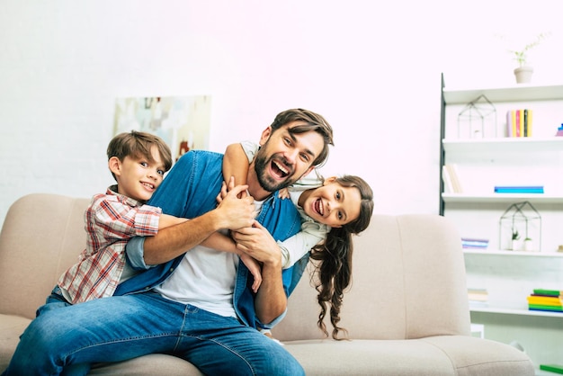 Handsome dad playing with beautiful happy kids on the couch at home