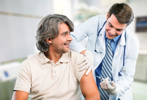 Handsome doctor making vaccination to male patient on background