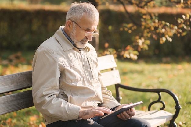 Handsome elderly man sitting on the bench and use tablet for scrolling in internet