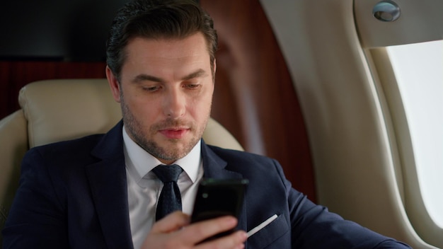 Handsome entrepreneur using smartphone in plane closeup Successful ceo travel