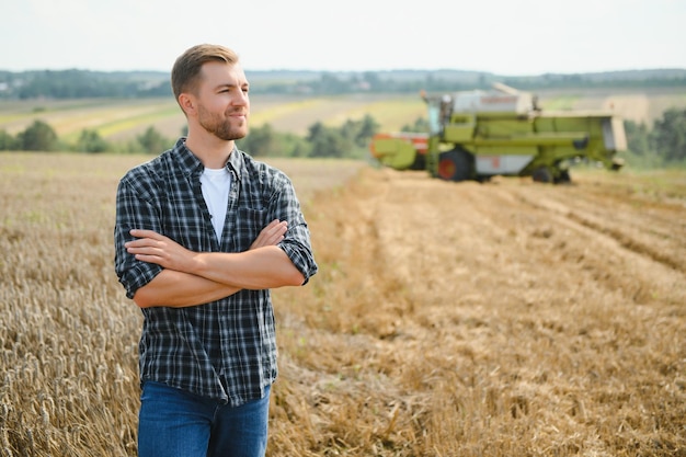 Handsome farmer with tablet standing in front of combine harvester during harvest in field