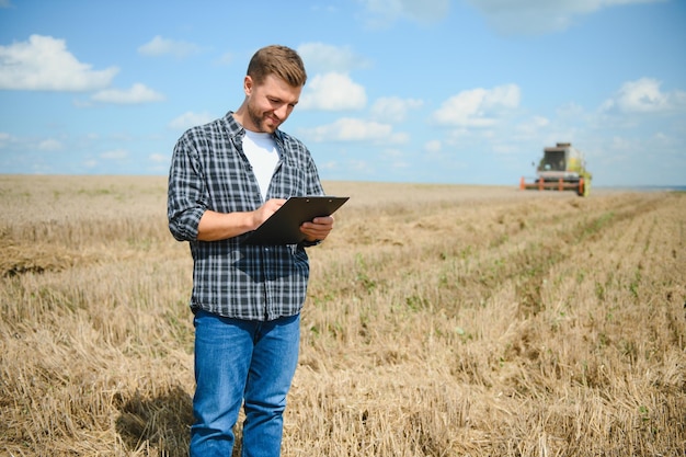 Handsome farmer with tablet standing in front of combine harvester during harvest in field