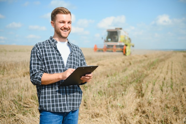 Handsome farmer with tablet standing in front of combine harvester during harvest in field