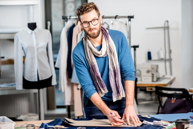 Handsome fashion designer working with fabric at the studio full of tailoring tools