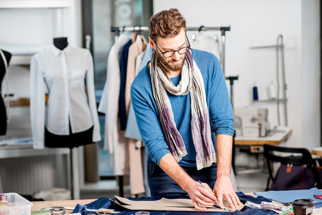 Handsome fashion designer working with fabric at the studio full of tailoring tools