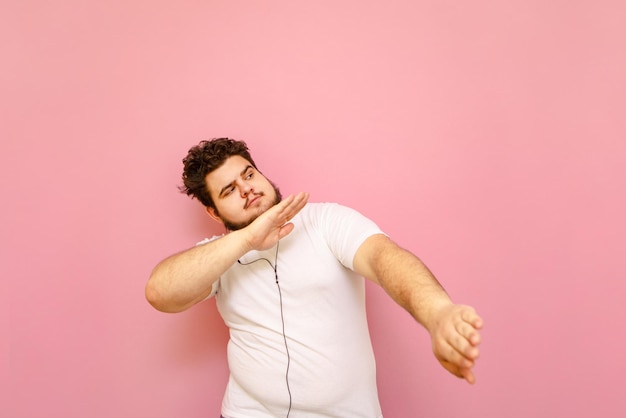 Handsome fat man listening to music in headphones and dancing on a pink background