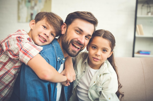 Handsome father is playing and have a fun with his little son and daughter at home on the couch. Happy family. Best father