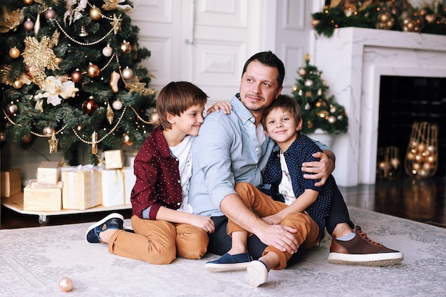 Handsome father playing  with his funny sons next to the  Christmas tree at home