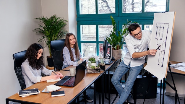 Handsome firm manager in glasses explains work tasks for his employees. Creative people or advertising business concept. Team work. Young beautiful people working in office together.