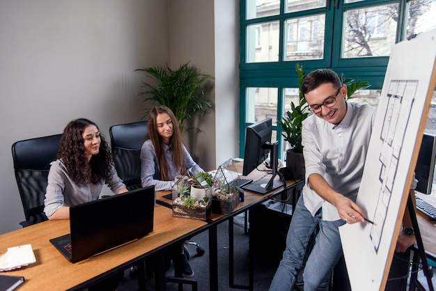 Handsome firm manager in glasses explains work tasks for his employees. Creative people or advertising business concept. Team work. Young beautiful people working in office together.