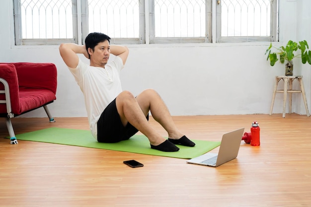 Handsome fitness man in a tshirt and shorts doing abdominal exercises on floor at home