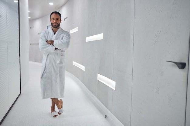 Handsome gentleman in white bathrobe looking at camera and smiling while crossing arms over his chest