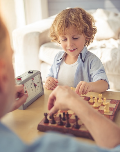 Handsome grandpa and grandson are playing chess and smiling.