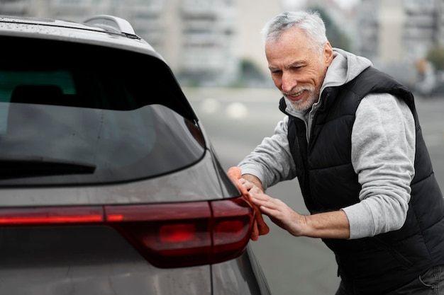 Handsome grayhaired senior man washing and polishing his car outdoors Car detailing concept